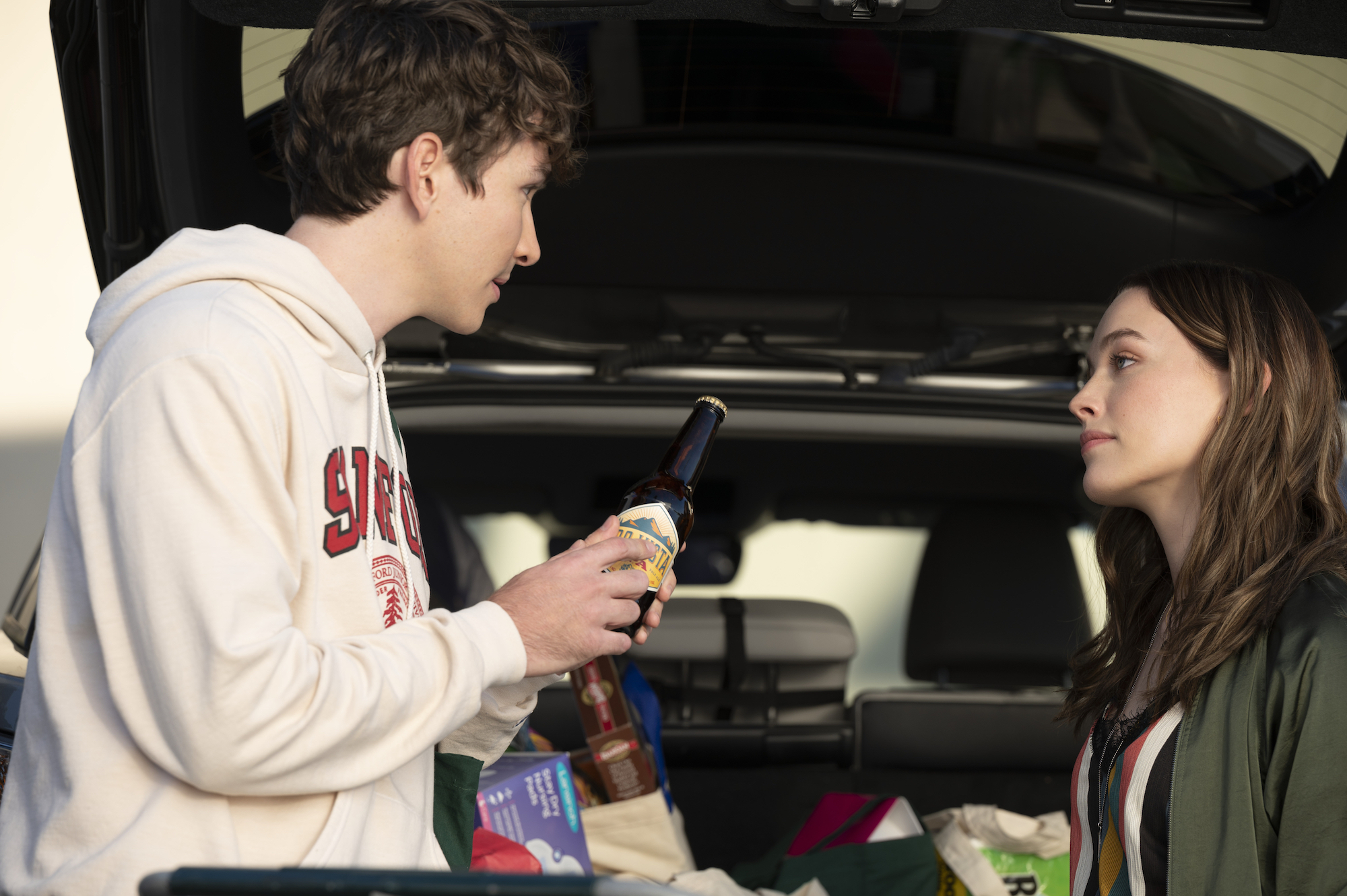 Dylan Arnold, and Victoria Pedretti talking near a car trunk in 'You' Season 3.