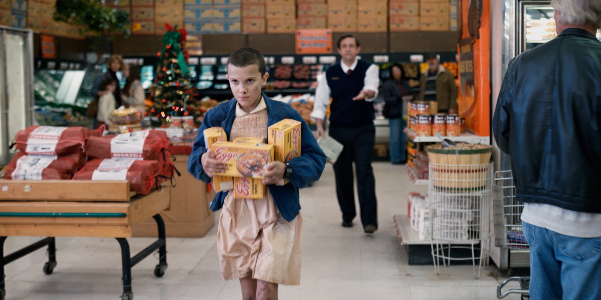 Eleven from 'Stranger Things' in Season 1 in a pink dress and navy jacket with a box of Eggos.