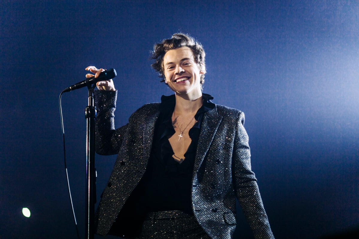 Harry Styles smiling and holding a microphone on stage