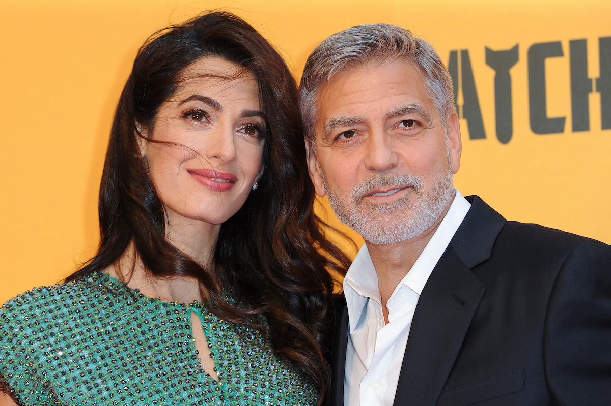 Amal and George Clooney smile and pose together at an event.
