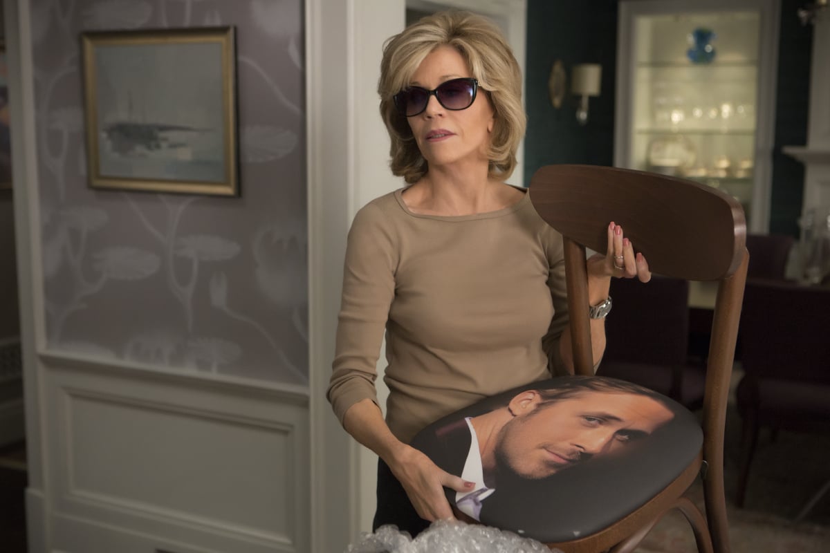 Grace holds the Ryan Gosling chair in the pilot episode of 'Grace and Frankie.' She is wearing sunglasses and a tan shirt.