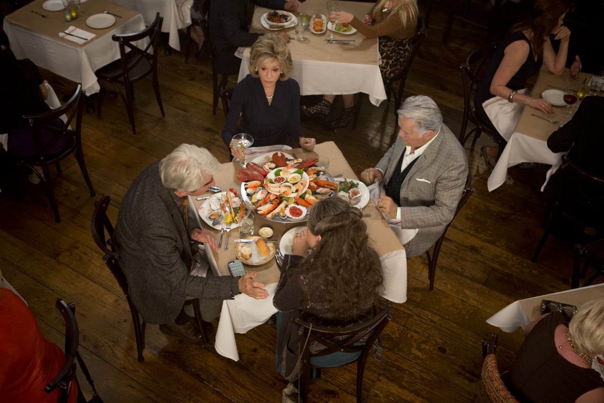 Grace, Frankie, Robert, and Sol sit around a table with seafood platter on it in the first episode of 'Grace and Frankie.'