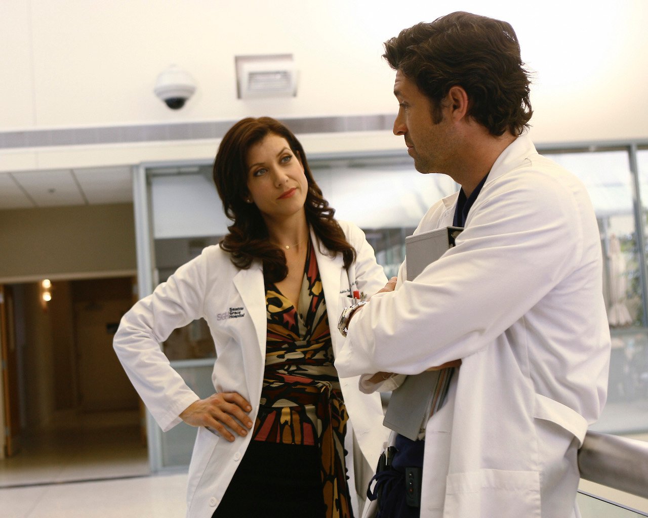 Kate Walsh as Addison Montgomery and Patrick Dempsey as Derek Shepherd on 'Grey's Anatomy' talk in their white coats in a hallway.