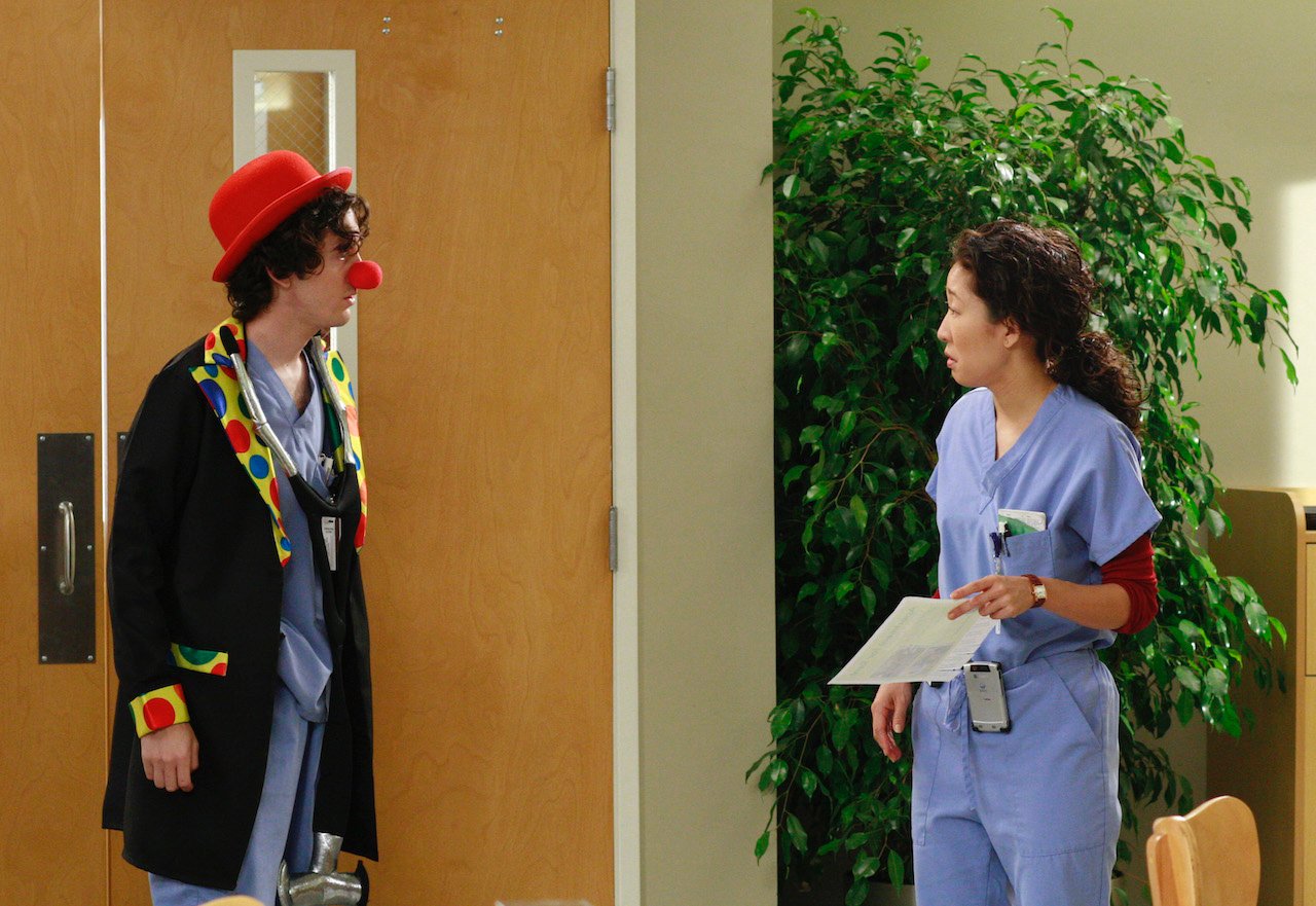 Sandra Oh as Cristina Yang on 'Grey's Anatomy' is in scrubs and is looking at a man dressed as a clown.