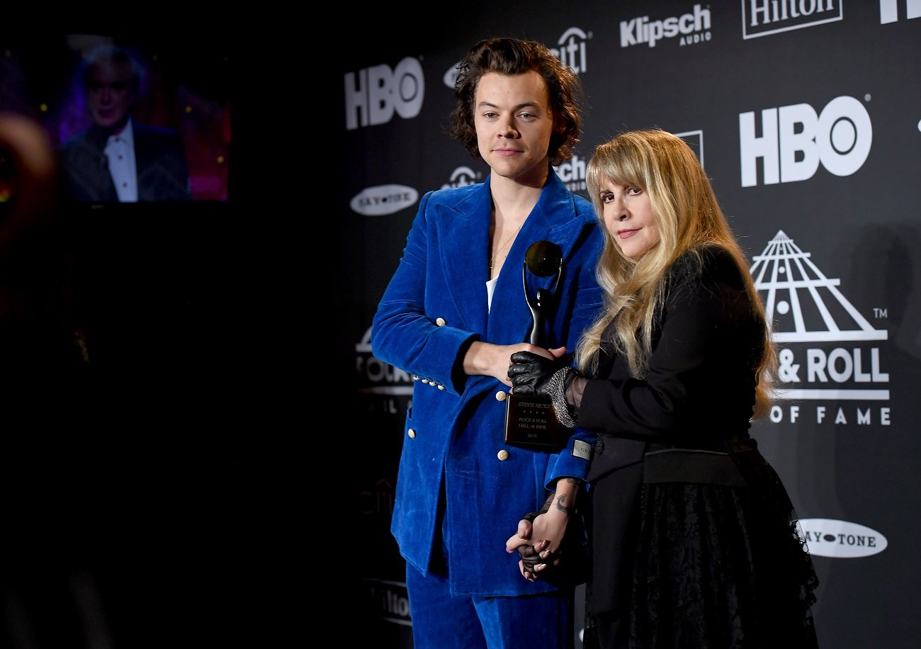 Harry Styles in a blue suit and Stevie Nicks in a black outfit. She holds an award.