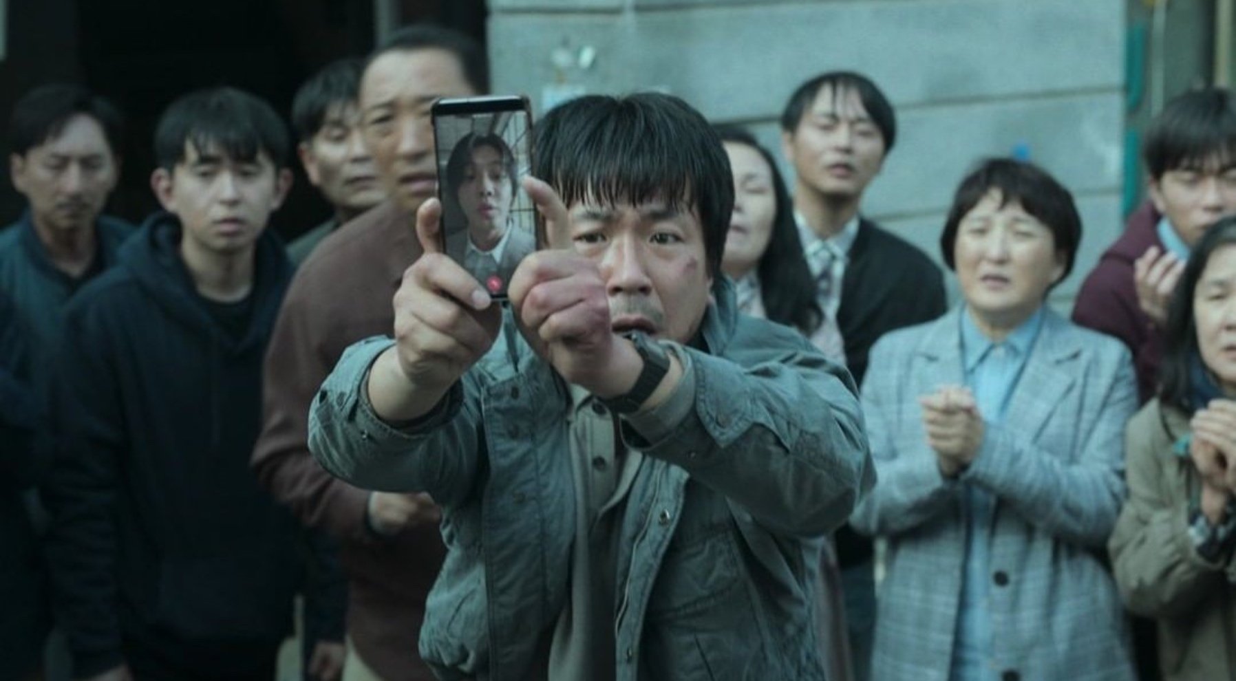'Hellbound' Netflix K-drama still image of man holding up cellphone to the public.