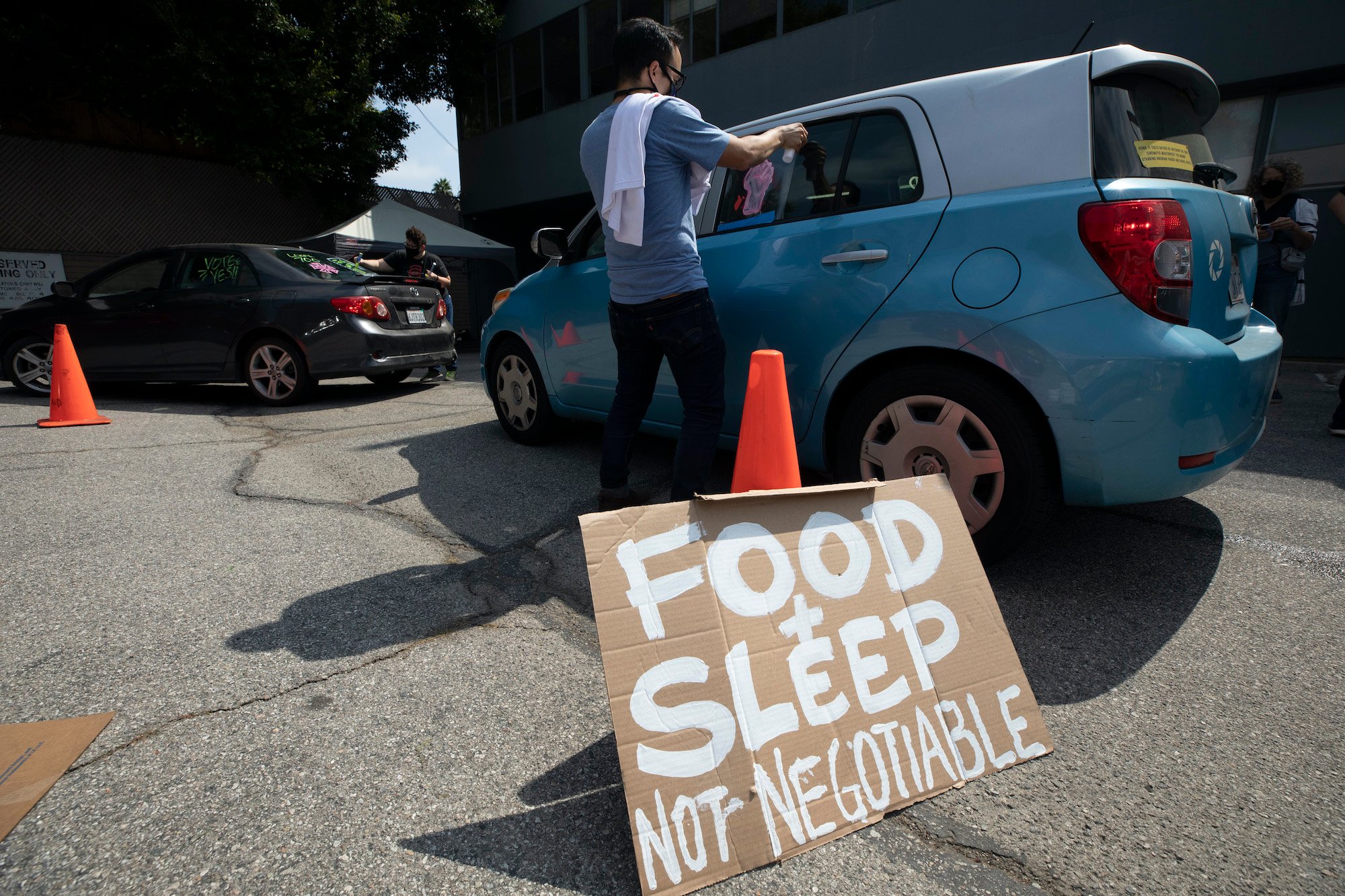 Hollywood union members a rally at the Motion Pictures Editors Guild IATSE Local 700 on Sunday, Sept. 26, 2021. One person puts a decal on a car window. A cardboard sign attached to an orange traffic cone that reads 'FOOD + SLEEP NOT NEGOTIABLE' is in the foreground. Up to 60,000 members of the IATSE might go on strike following the IATSE strike vote on Oct. 1.