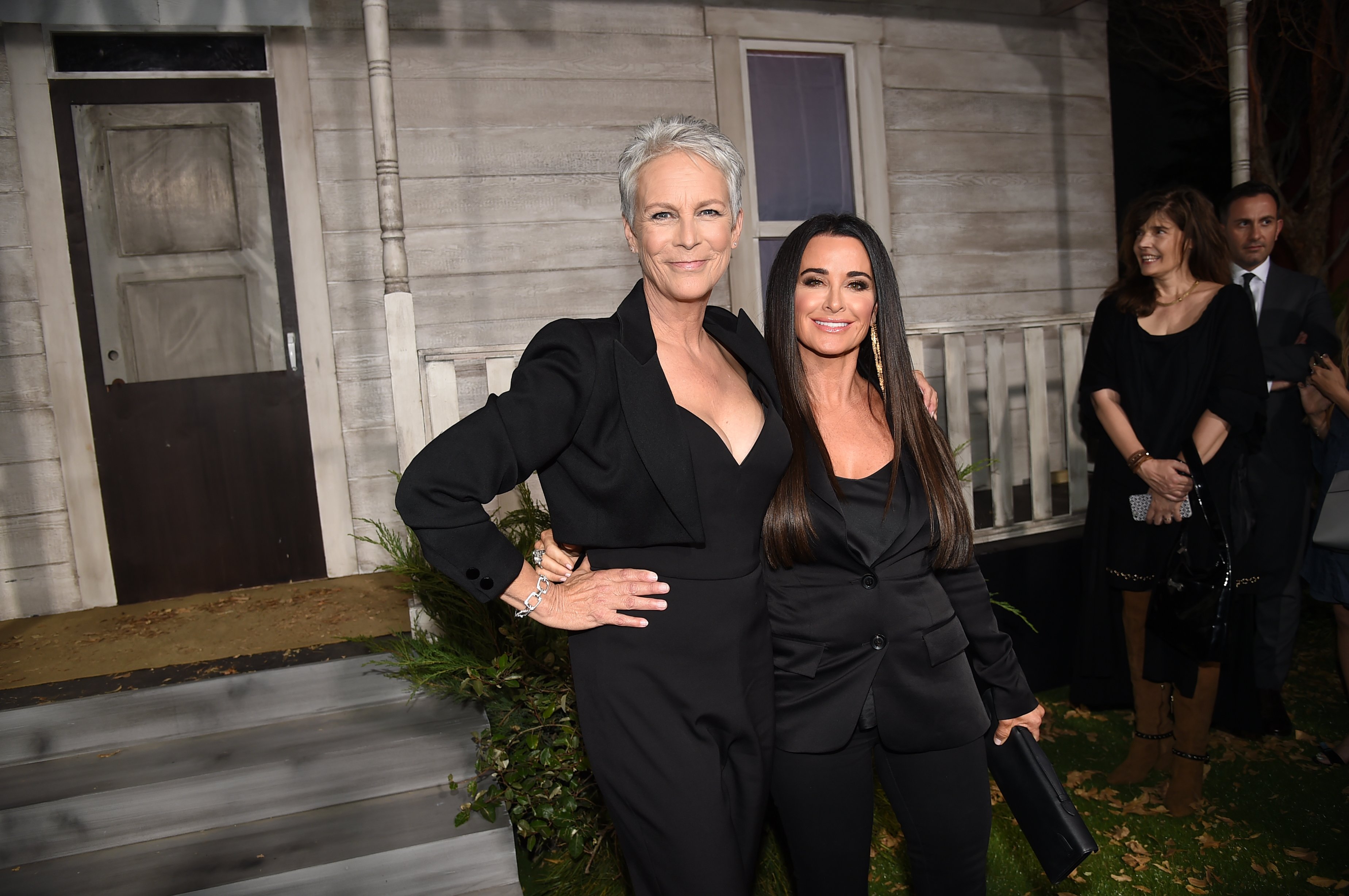 Halloween Kills actors Jamie Lee Curtis and Kyle Richards wear black and pose together in front of a house.