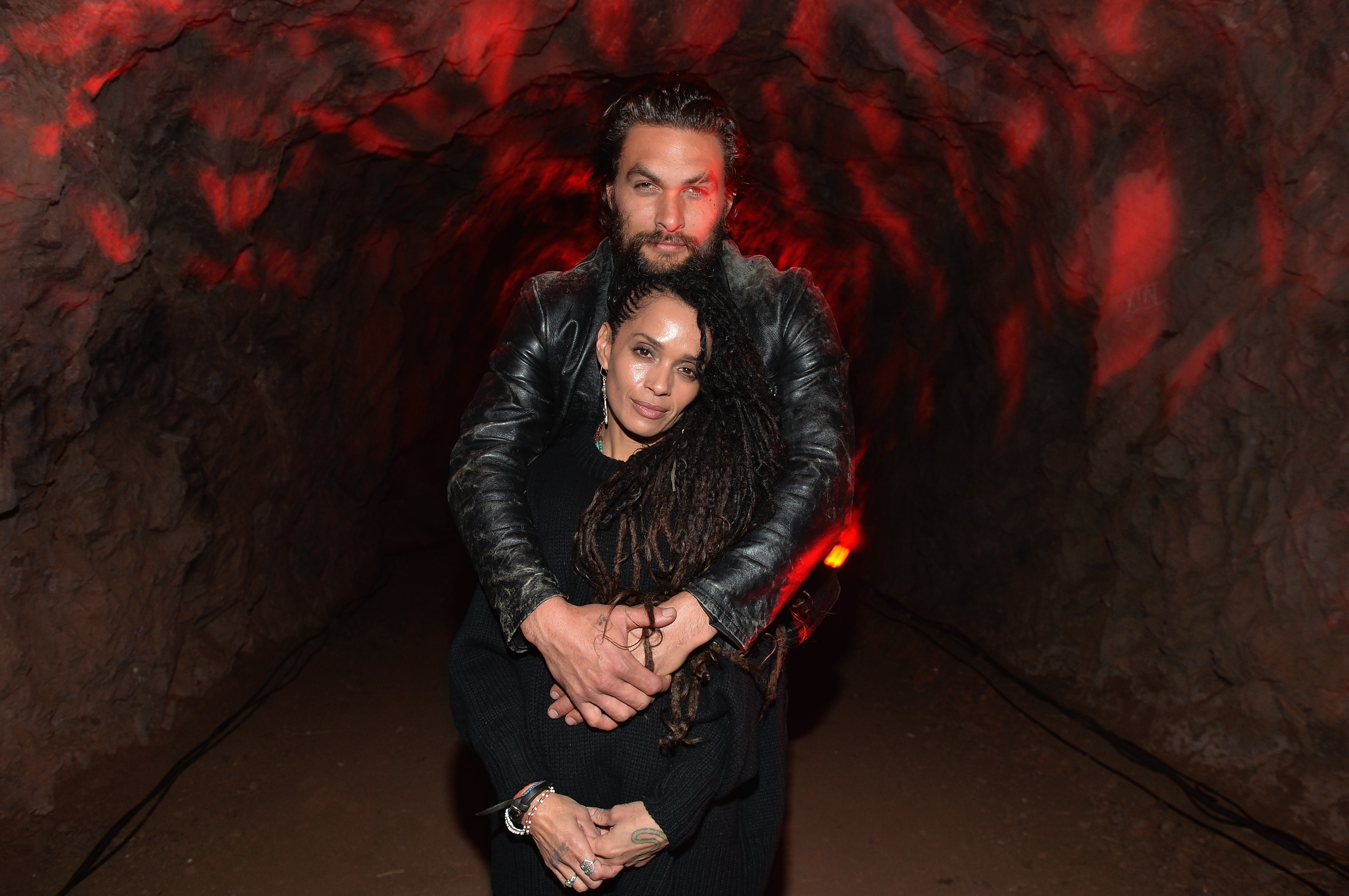 Lisa Bonet and Jason Momoa embrace while standing in front of a dark background.