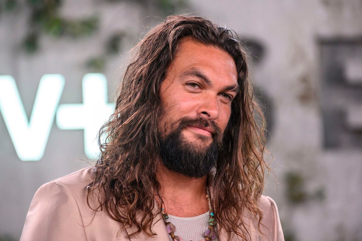 Jason Momoa smiling in front of a blurred background