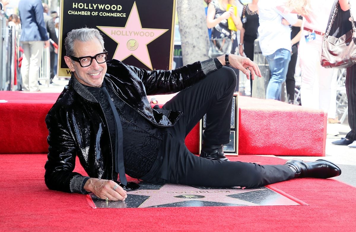 Jeff Goldblum wearing glasses and dressed in black, reclined with hand rested on knee