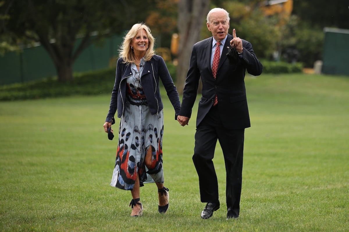 Jill Biden and Joe Biden hold hands and walk across a grassy lawn together.