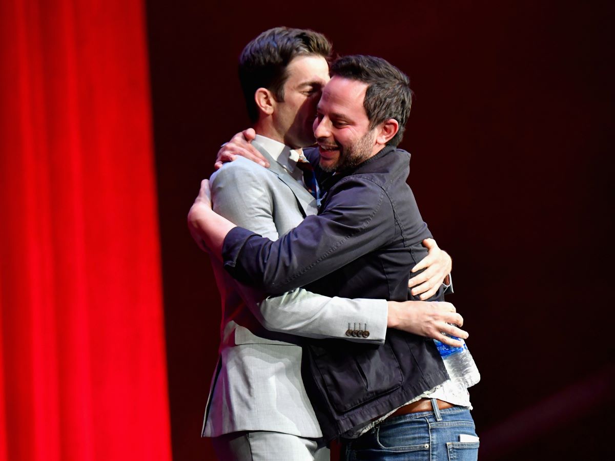 John Mulaney whispers into a smiling Nick Kroll's ear