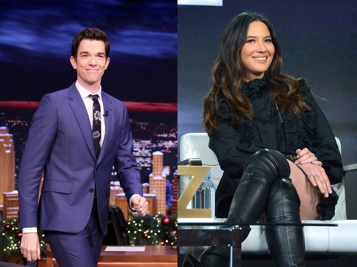 John Mulaney on left in a blue suit, walking. Olivia Munn on right, seated in all black