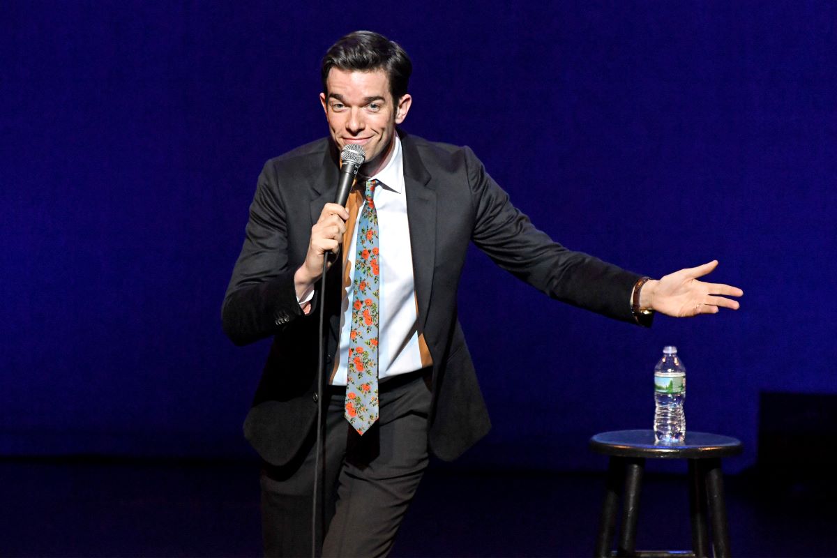 John Mulaney in a floral tie, holding a microphone