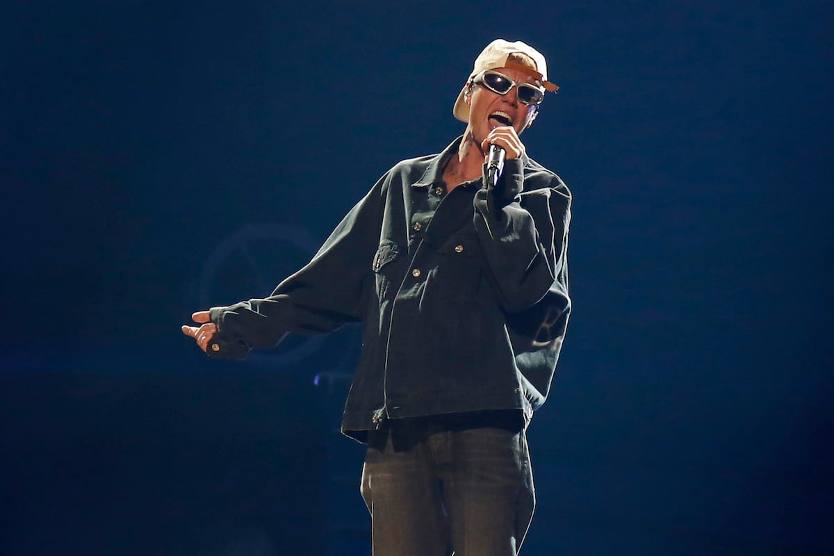 Justin Bieber performs on stage wearing a backwards cap and sunglasses.