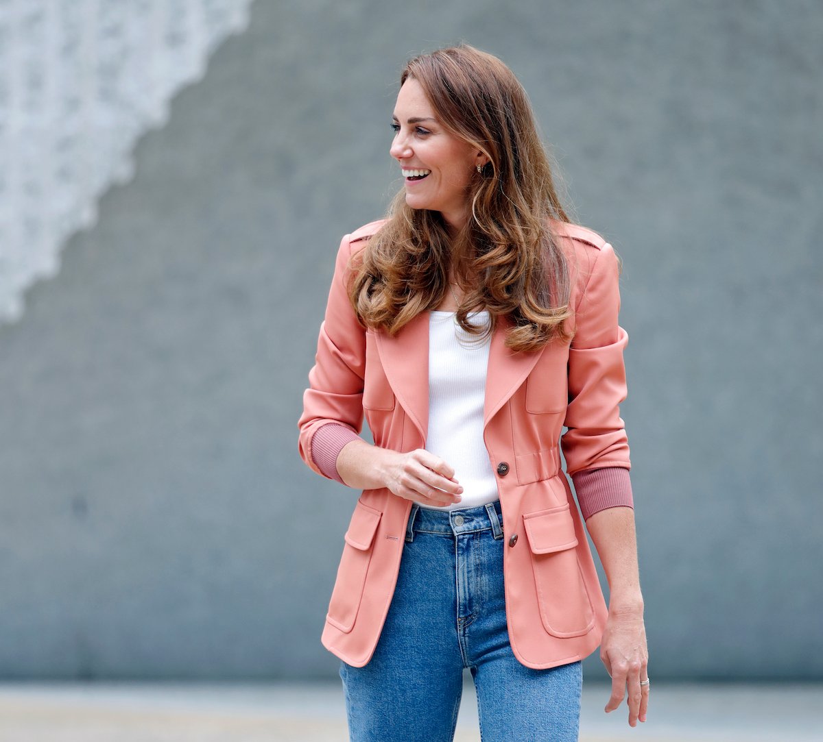 Kate Middleton laughing, turned to the right, wearing a pink blazer, white shirt, and high waisted jeans