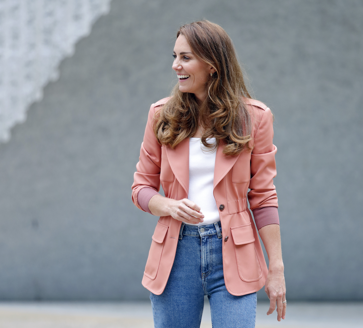 Kate Middleton laughing, facing right, wearing a pink blazer, white shirt and high waisted jeans