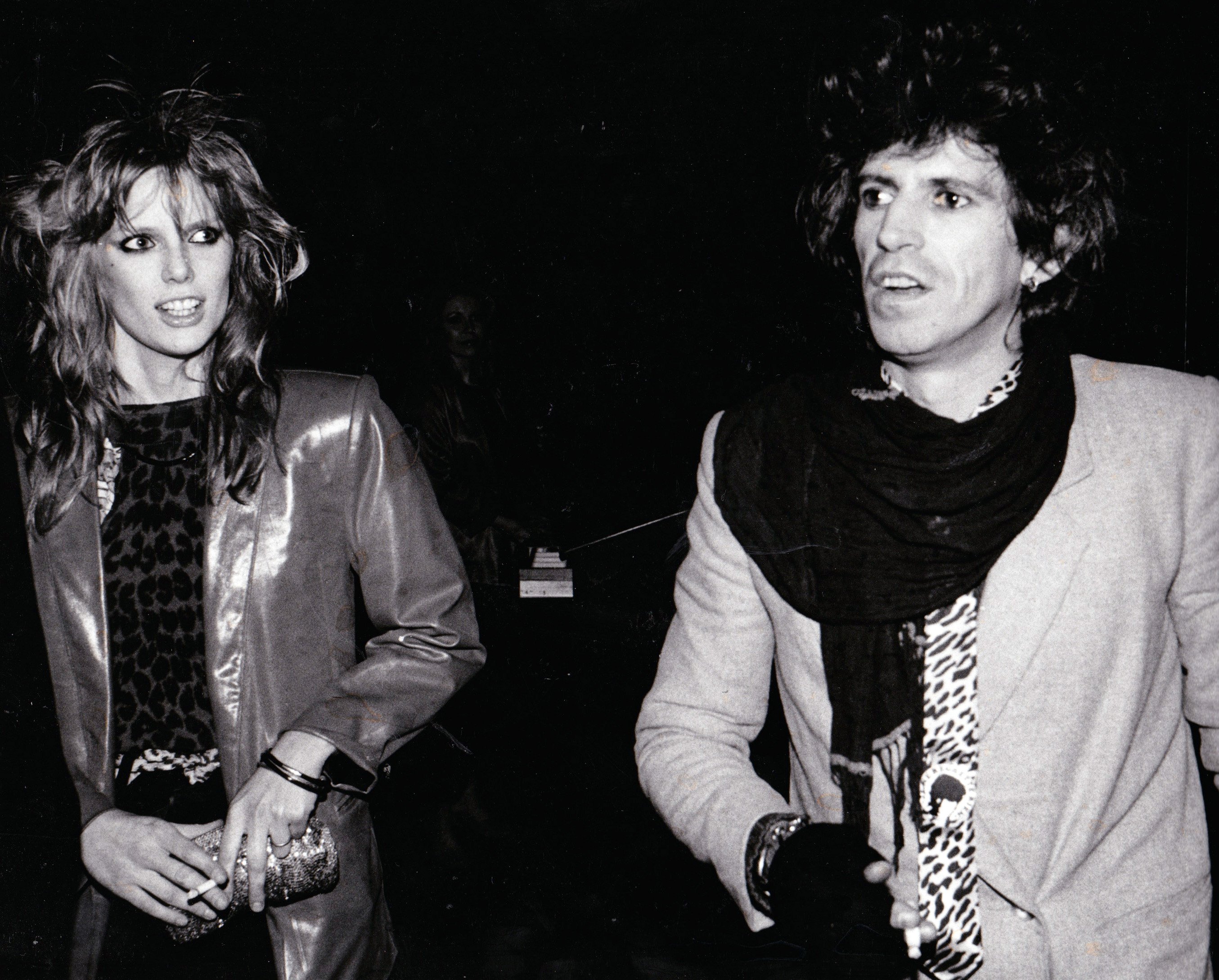 Patti Hansen and Keith Richards walk in front of a dark background.