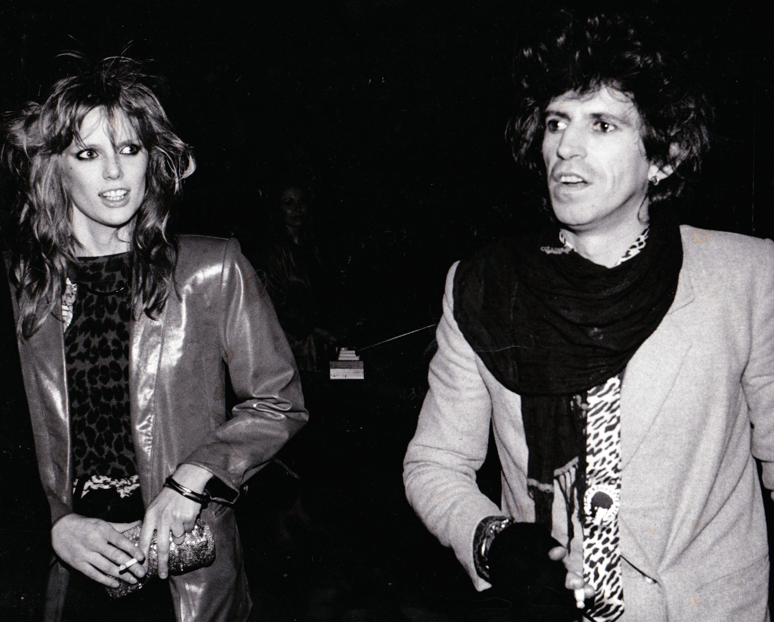 Patti Hansen and Keith Richards walk in front of a dark background. 