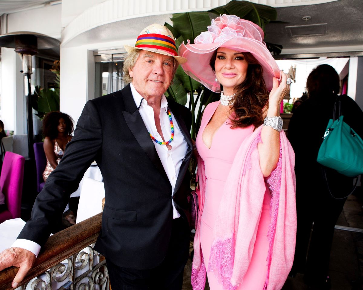 Ken Todd in suit and hat, Lisa Vanderpump in pink dress and matching hat, standing close to each other