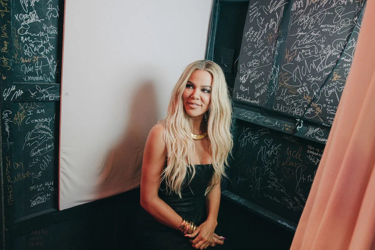 Khloe Kardashian sitting down while wearing a black dress.