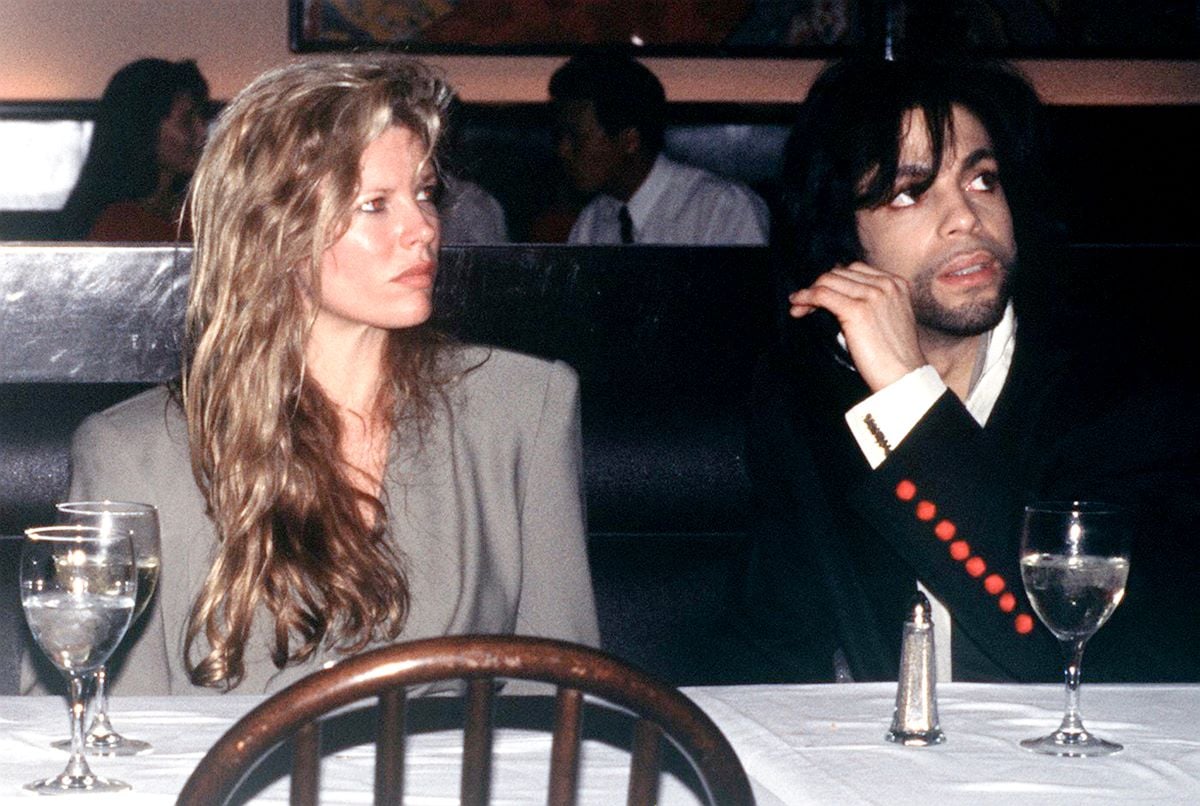 Kim Basinger and Prince sit at a table together, looking away from camera