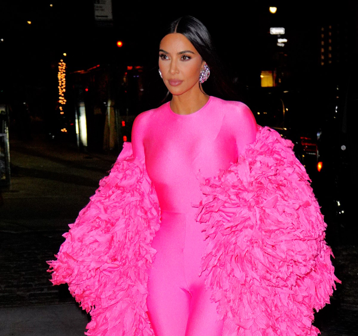 Kim Kardashian West arrives at the afterparty for Saturday Night Live. She is wearing a pink catsuit with large earrings and a pink feather wrap.