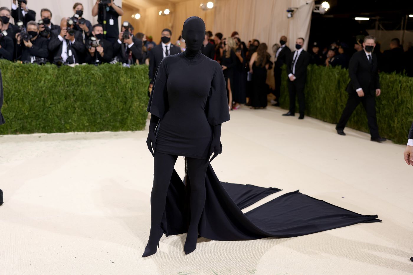 Kim Kardashian West in her famous Met Gala black outfit on the red carpet with photographers behind her.