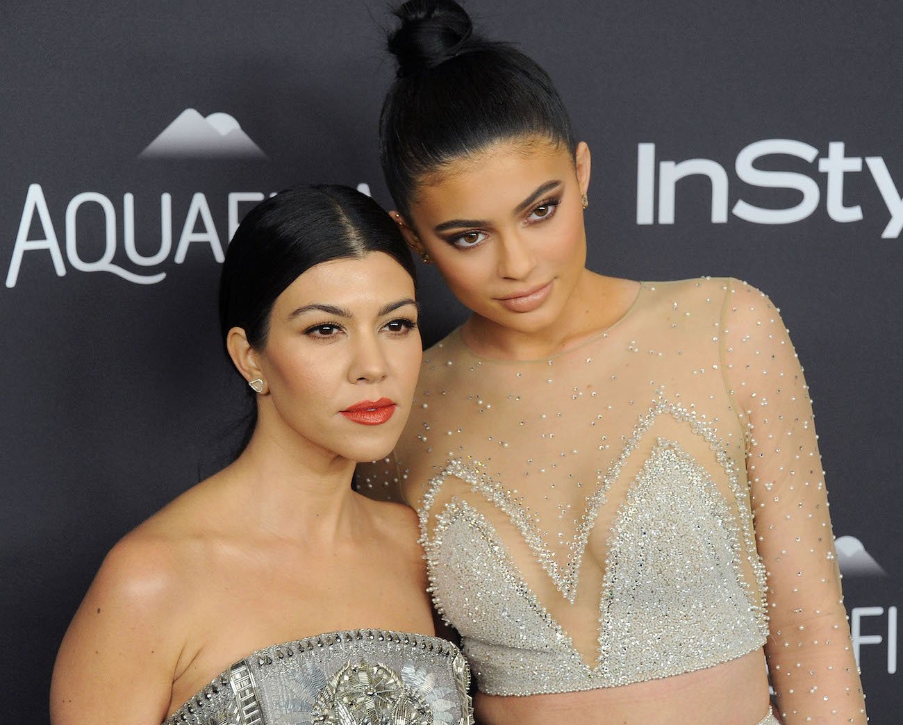 Kourtney Kardashian and Kylie Jenner standing next to each other in front of dark background