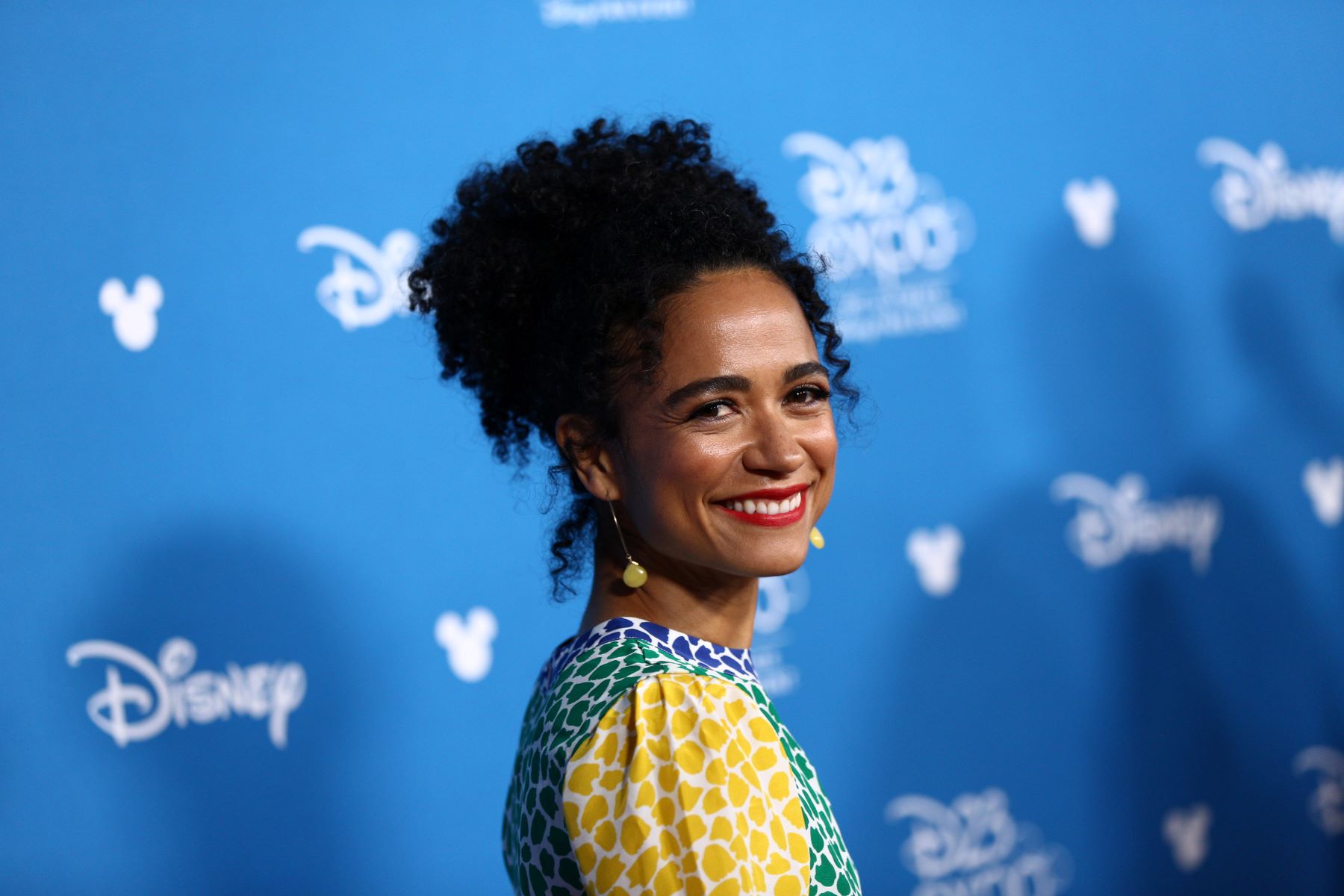 Marvel's 'Eternals' star Lauren Ridloff wears a yellow, green, and blue dress and dangly earrings.