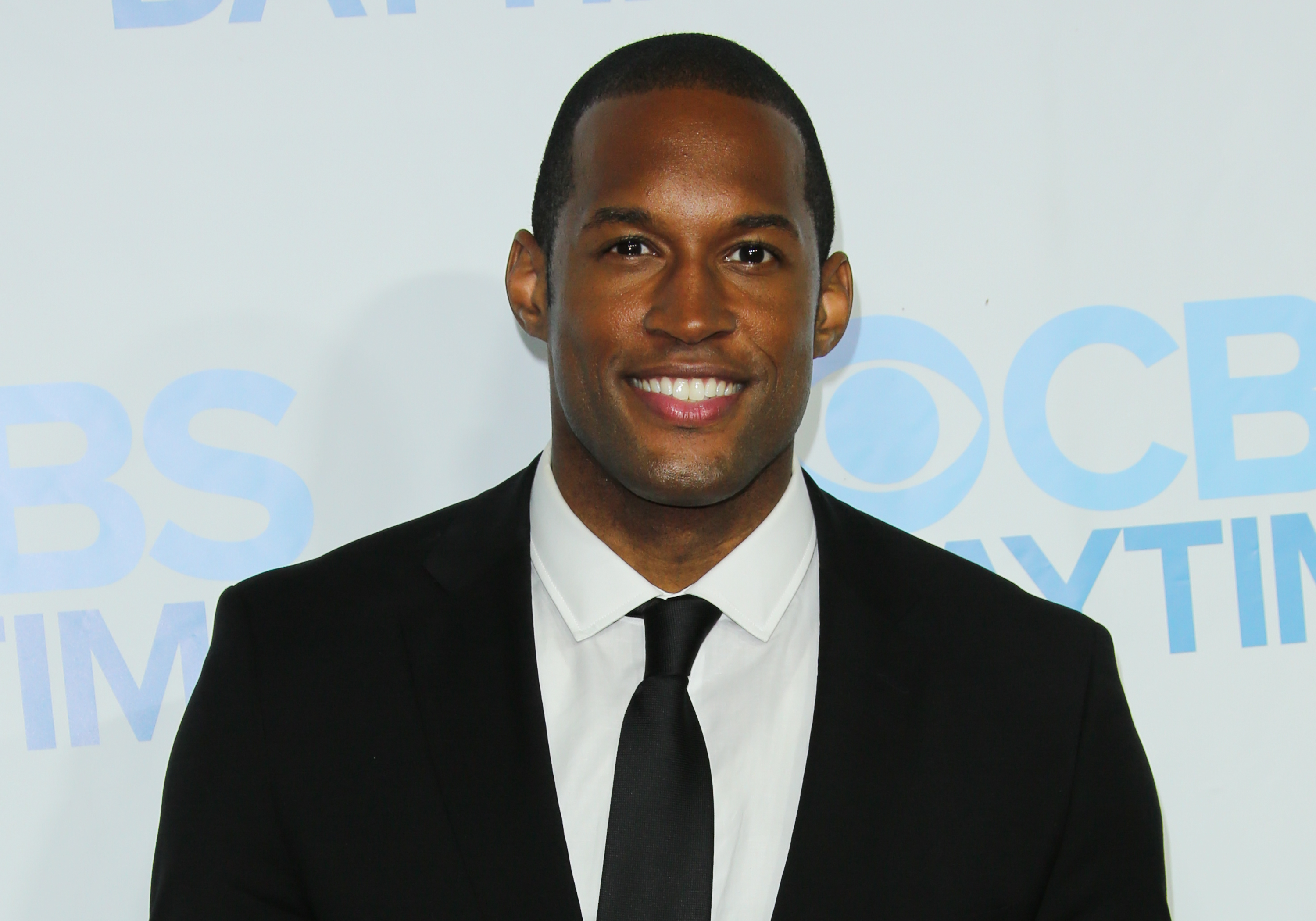 'The Bold and the Beautiful' actor Lawrence Saint-Victor in a black suit and tie, and a white shirt smiling on the red carpet.