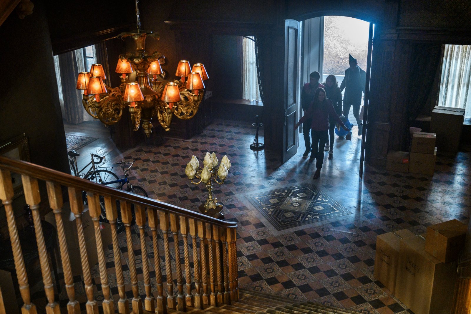 The Locke family arrives at Keyhouse in 'Locke & Key' Season 1 on Netflix. The entrance to the manor is dim, and fans can see a chandelier hanging overhead and a stairway