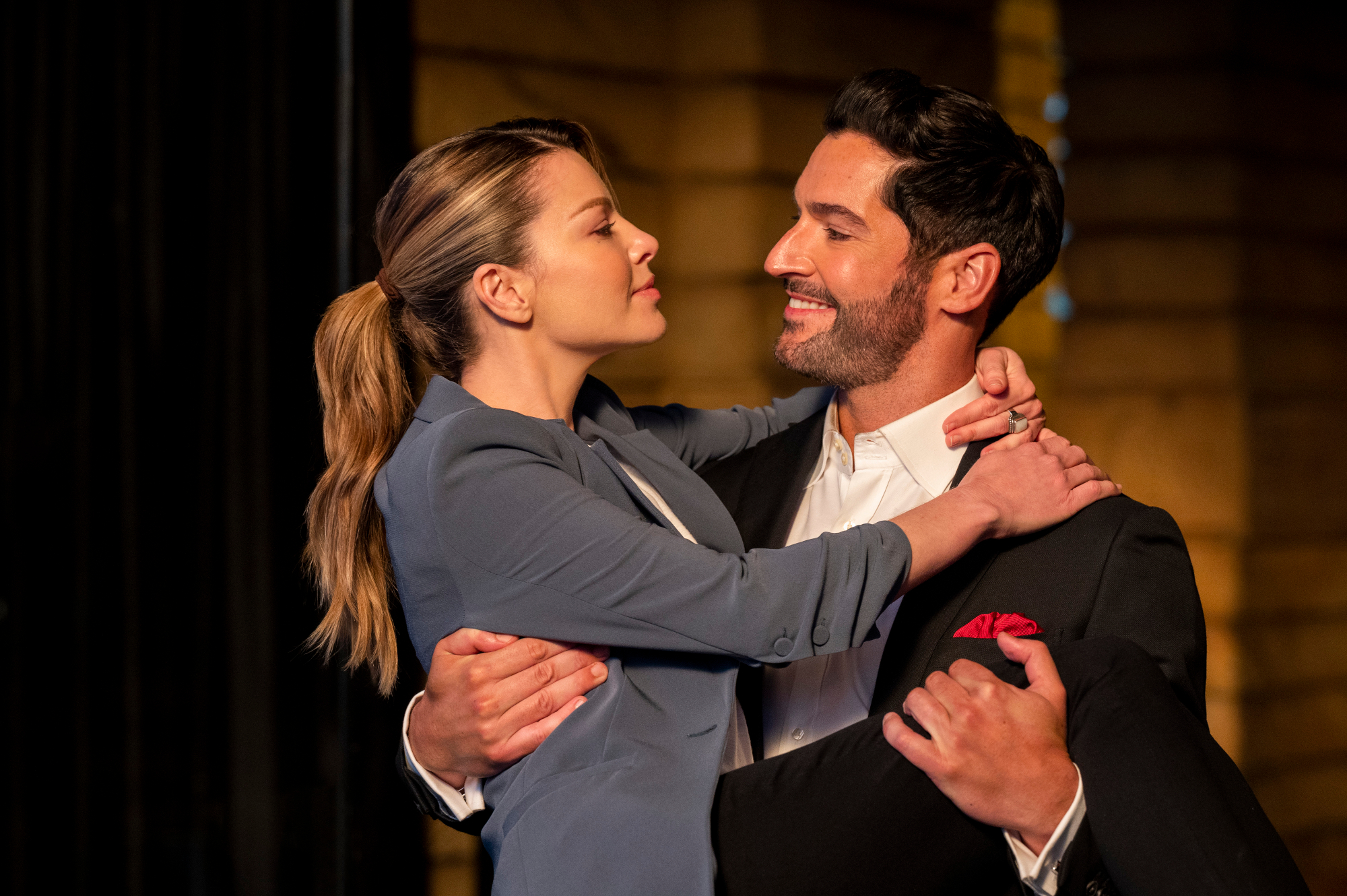 Lauren German and Tom Ellis as Chloe Decker and Lucifer Morningstar in 1 of the episodes from 'Lucifer' Season 6. He's bridal carrying her and they're smiling at one another.