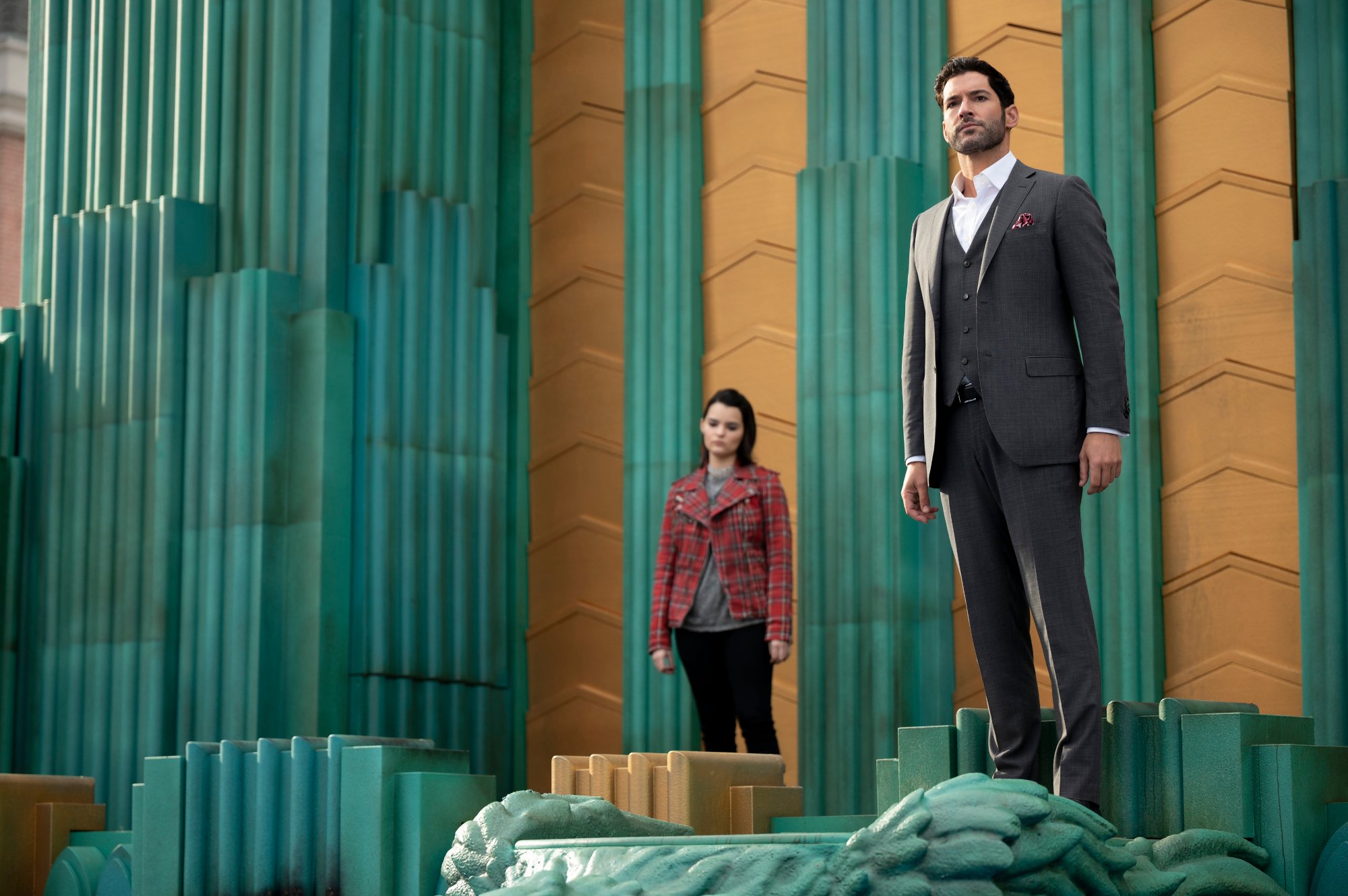 Tom Ellis and Brianna Hildebrand in 'Lucifer' Season 6. They're standing on a green and yellow surface and looking out at something.