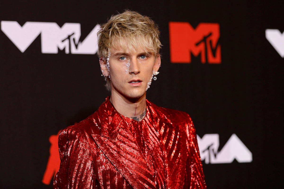Machine Gun Kelly wearing crystals and pearls on his face and a red sparkly suit.