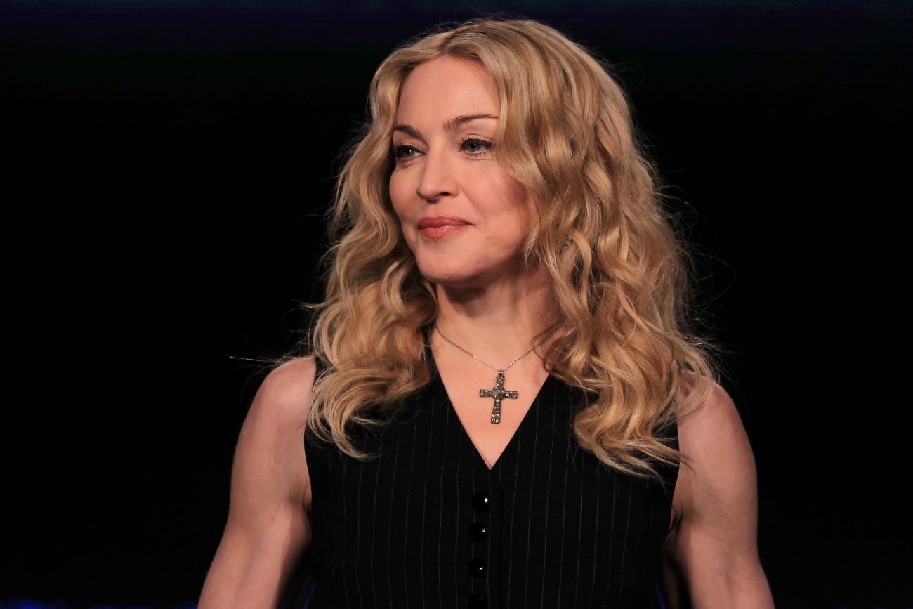 Madonna in a black tank top and cross necklace against a black background.