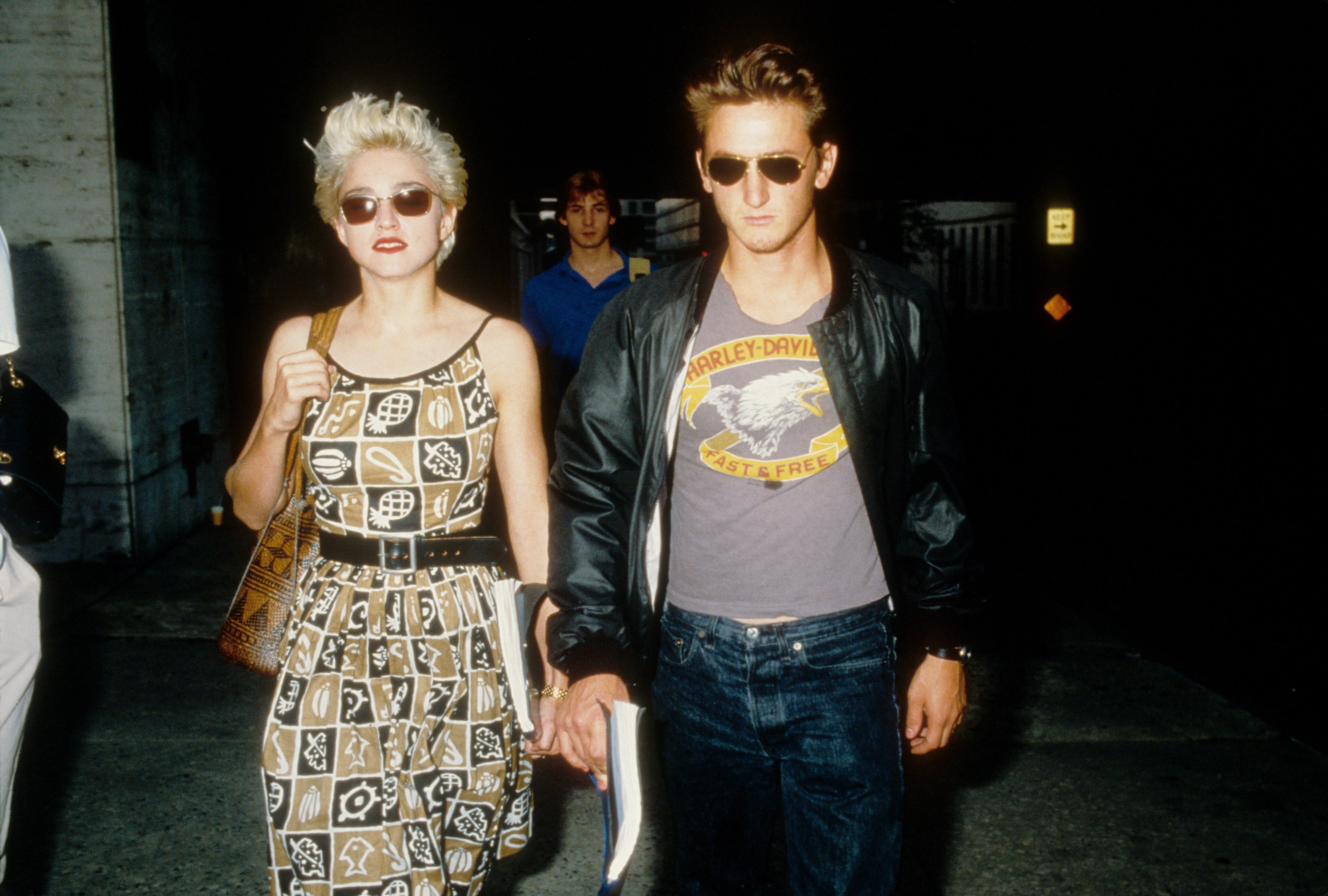 Madonna wears a tan and black patterned dress and Sean Penn wears a Harley Davidson shirt. they both wears sunglasses.