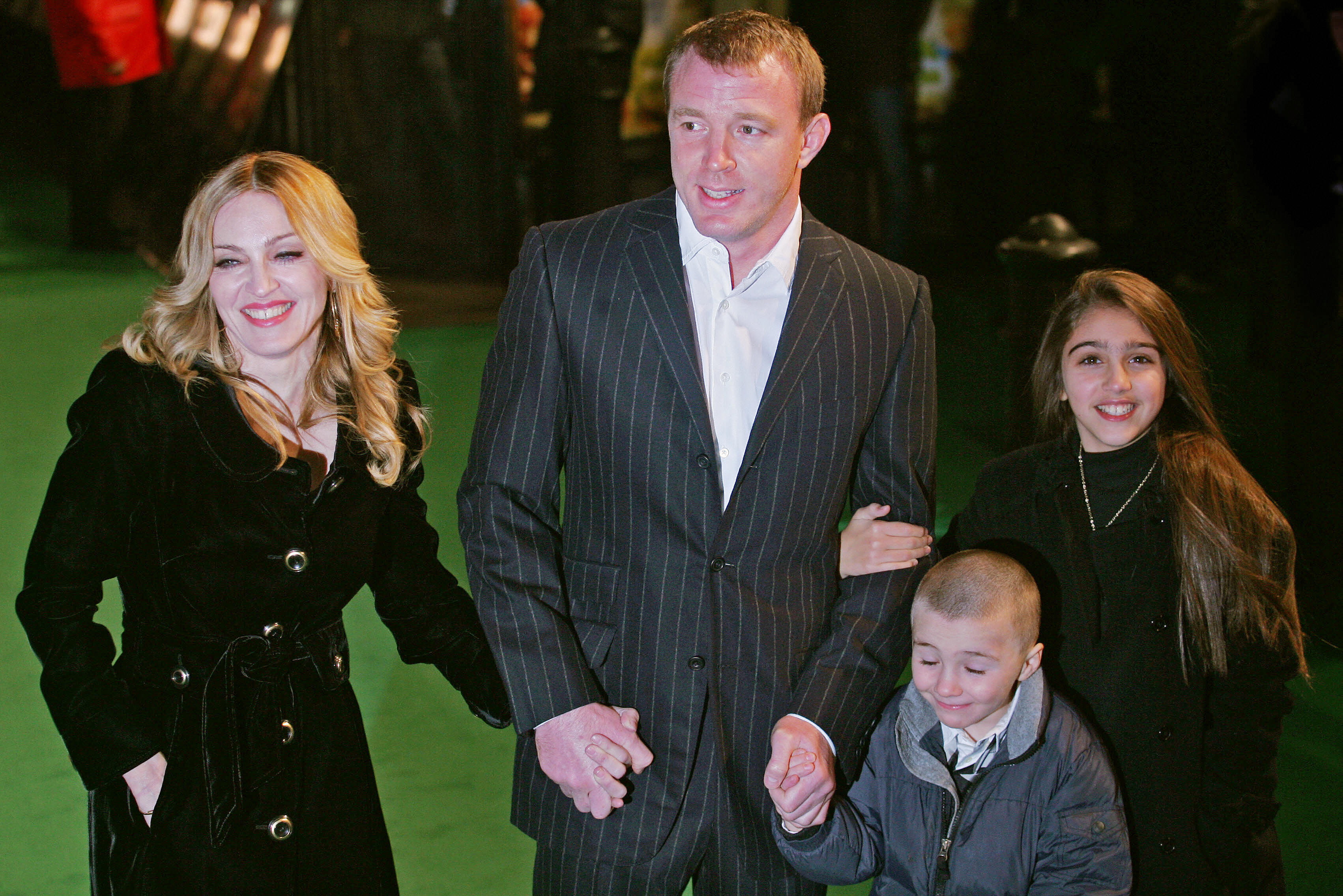 Madonna, Guy Ritchie, Rocco Ritchie, and Lourdes Leon wear black coats and hold hands.