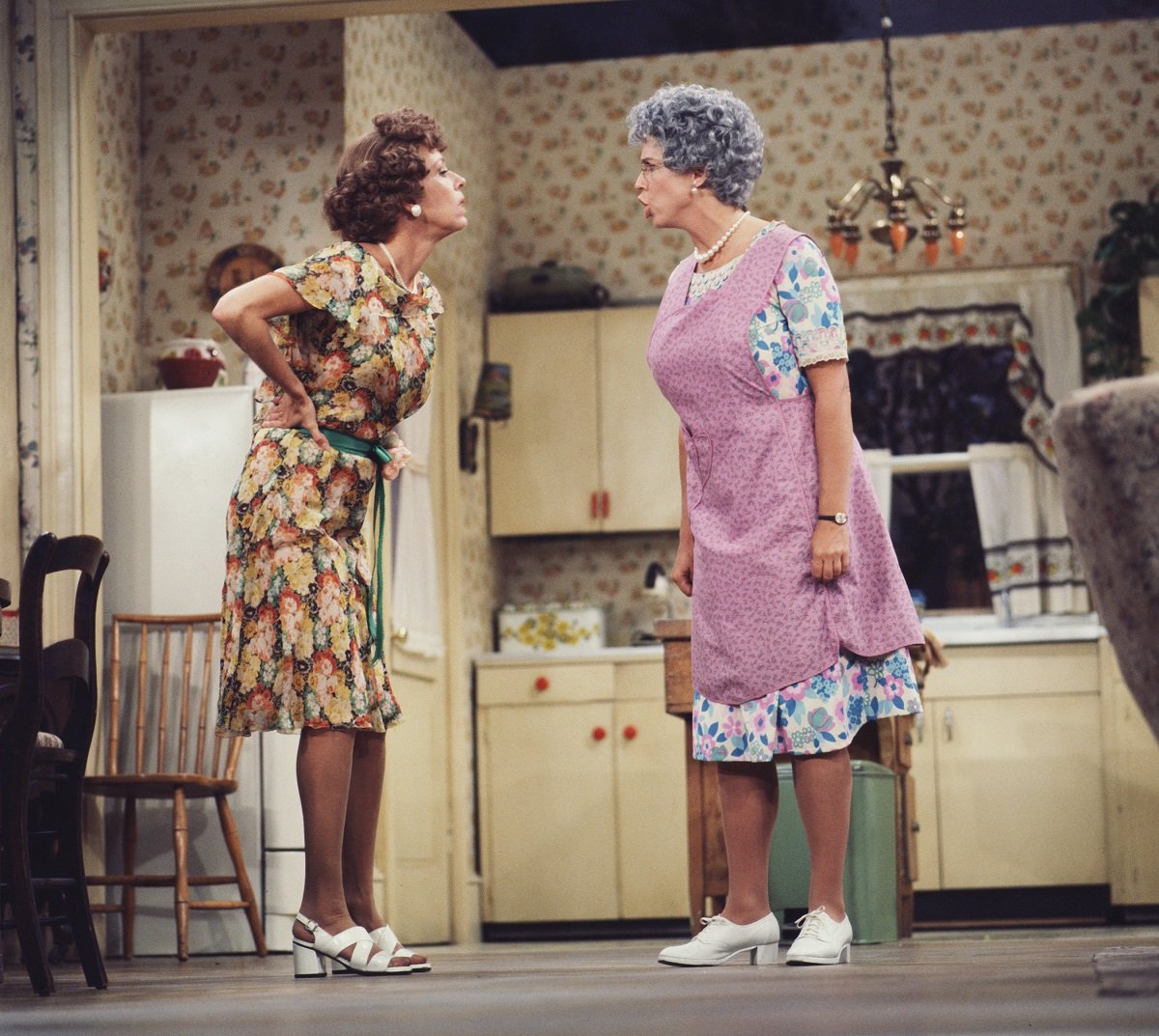 Carol Burnett wearing a green and orange floral dress, and Vicki Lawrence in a blue floral dress and purple apron film a scene for 'Mama's Family.'
