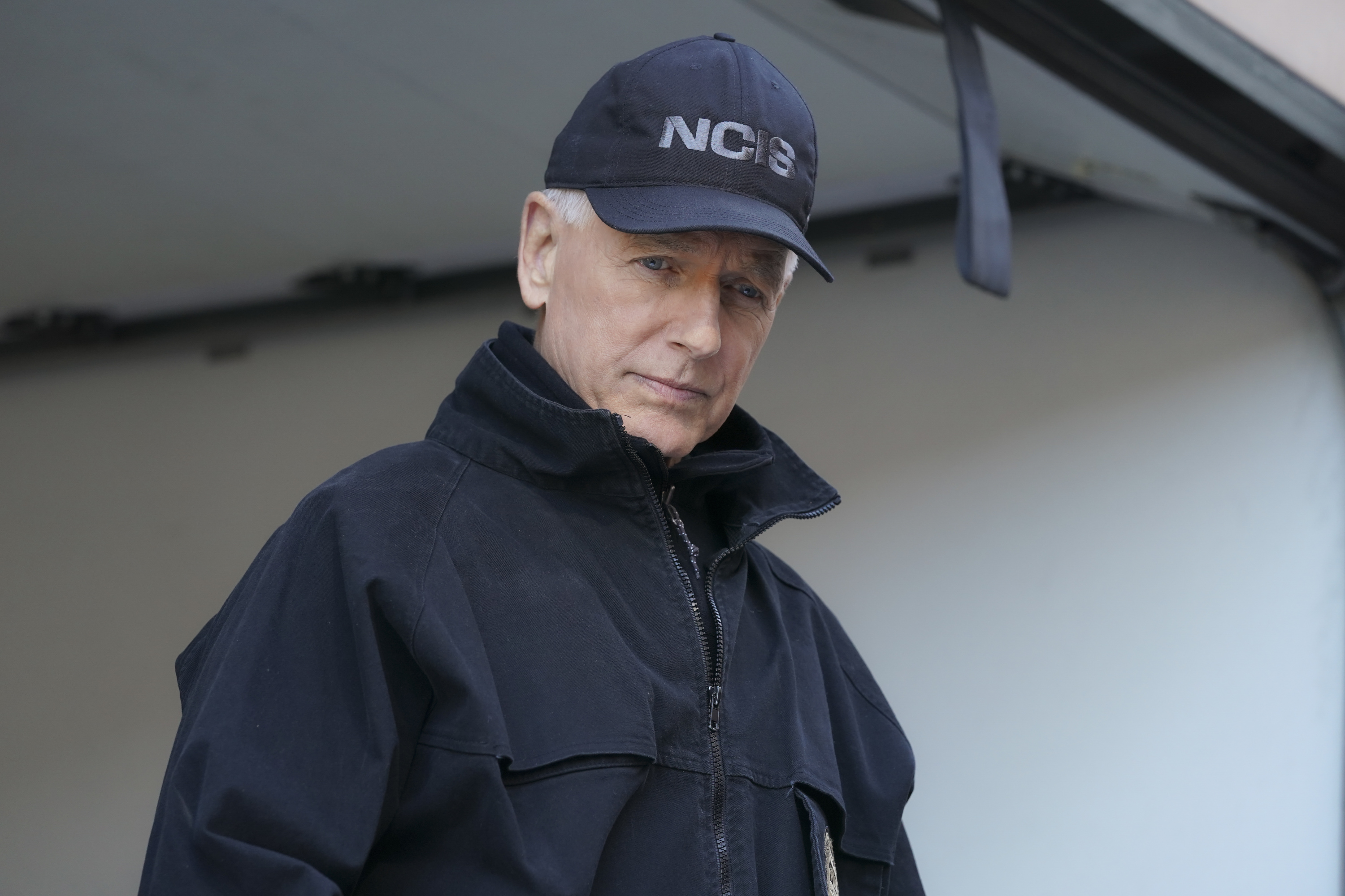 'NCIS' actor Mark Harmon in a black jacket and black NCIS hat filming a scene for the series.