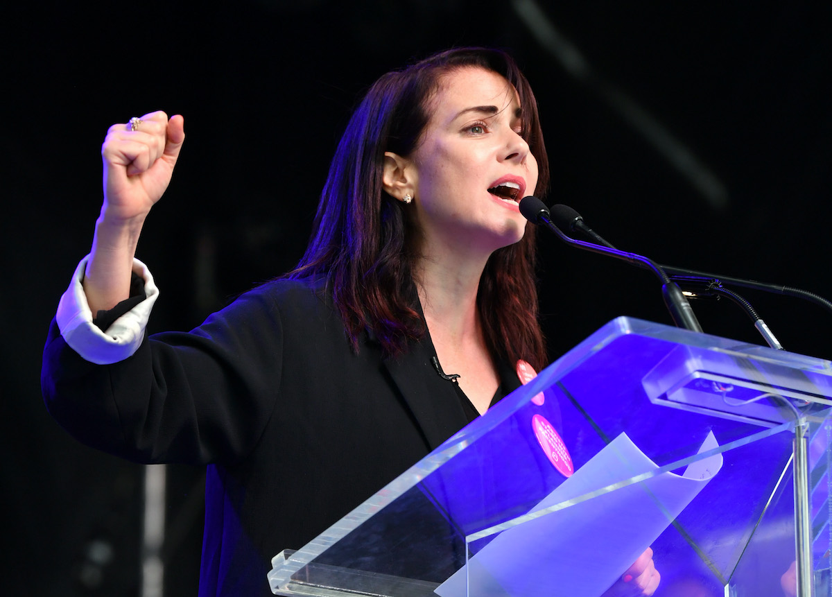 Mia Kirshner gives a speech at an industry event wearing a black outfit