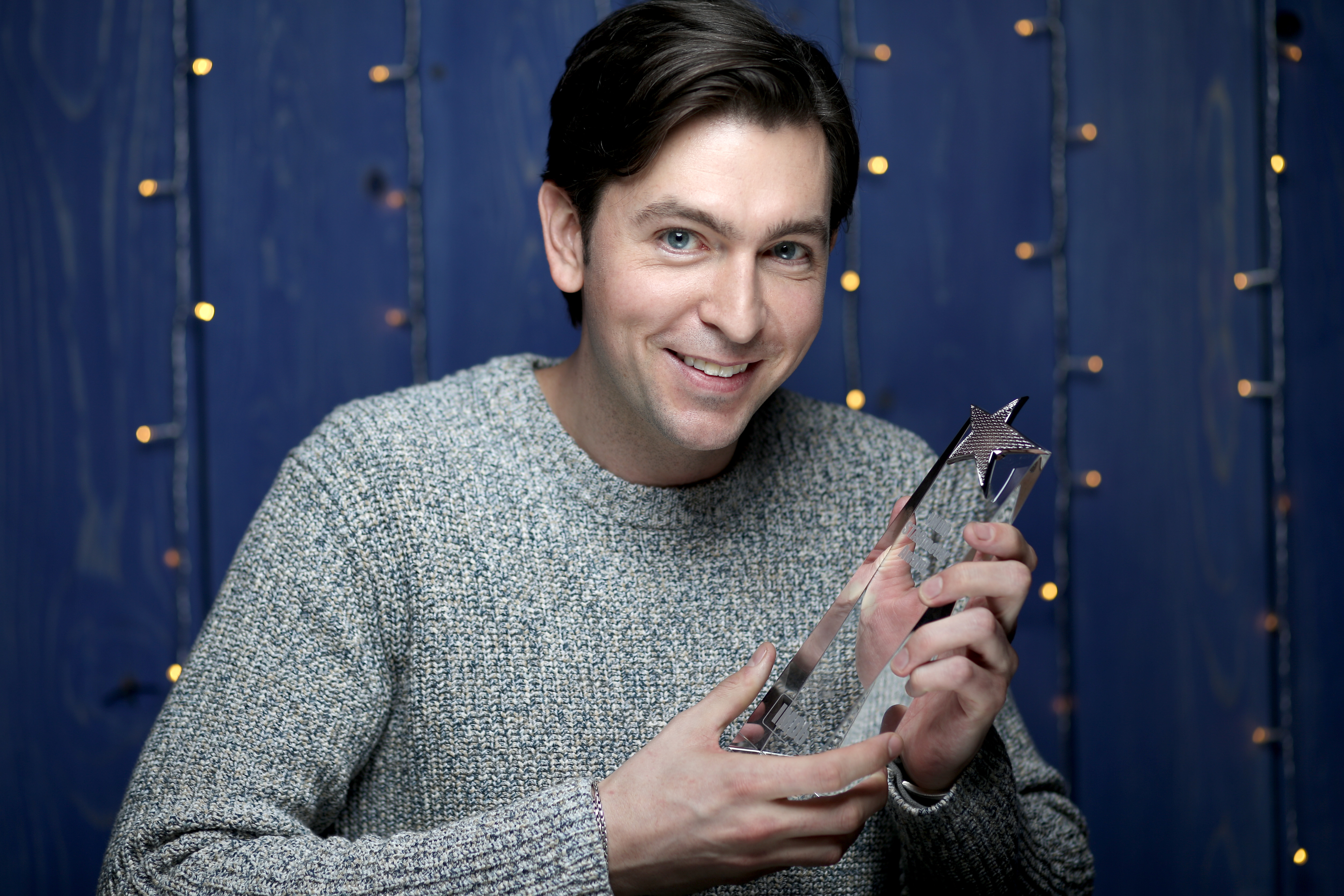 Succession Season 3 star Nicholas Braun in a gray sweater, holding an award.