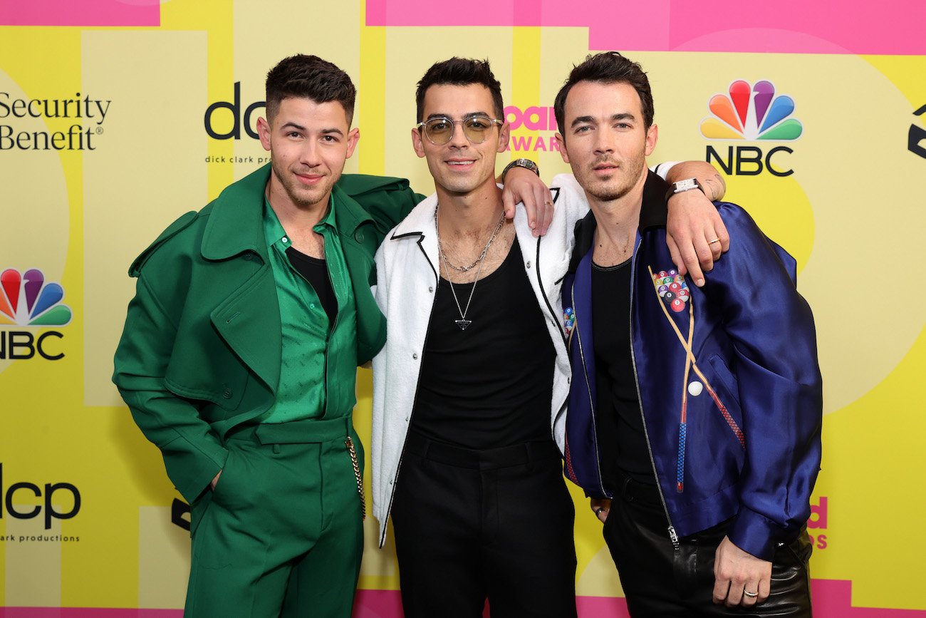Nick Jonas, Joe Jonas, and Kevin Jonas smile with their arms around each other at the 2021 Billboard Music Awards