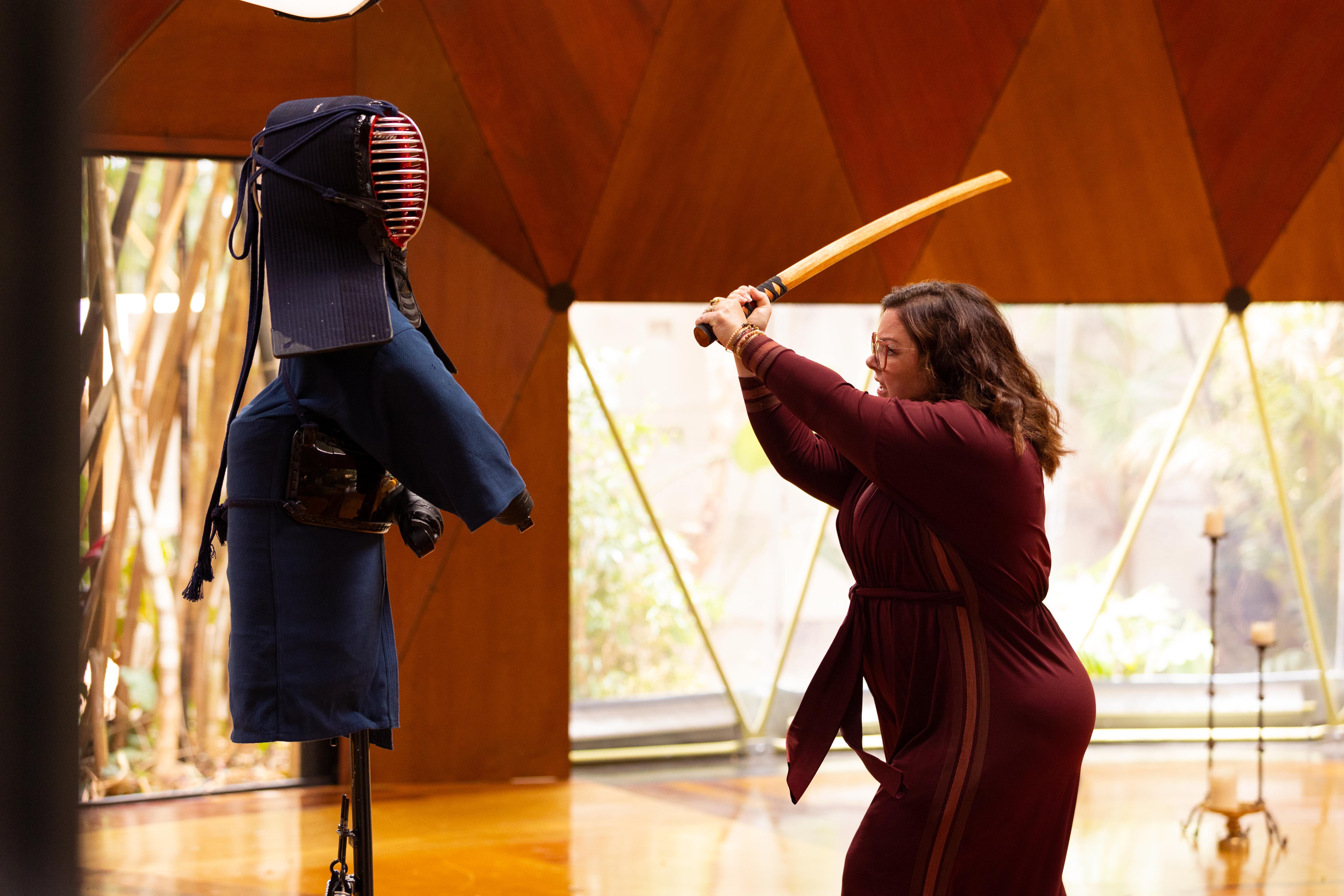 Melissa McCarthy as Frances Welty in 'Nine Perfect Strangers.' Frances attacks a dummy with a sword. She is wearing a red jumpsuit.