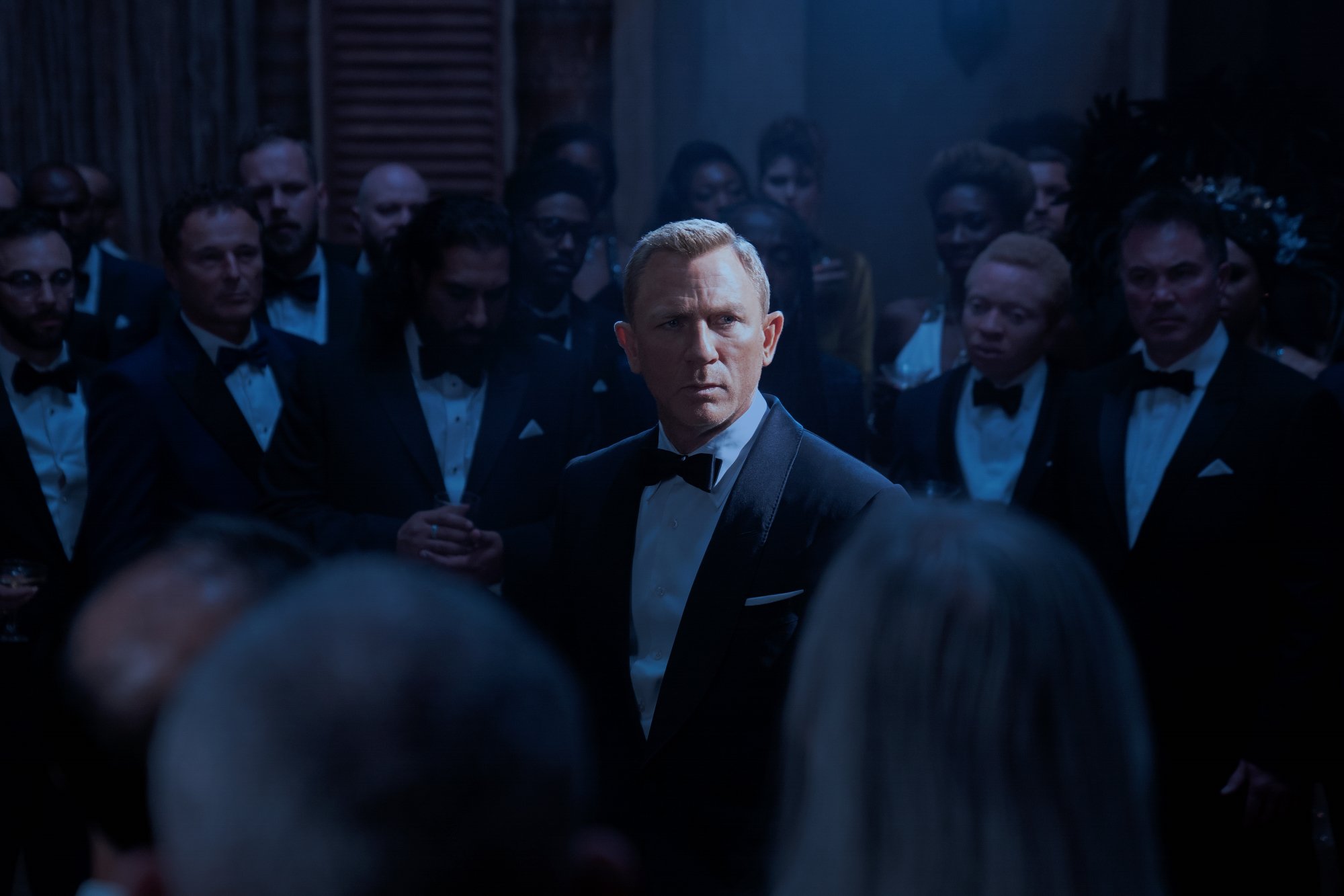 'No Time to Die' Daniel Craig James Bond wearing a suit standing in the middle of a crowd with a spotlight on him