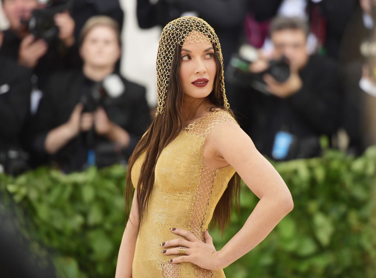 Olivia Munn poses with hand on hip in gold dress and gold headpiece