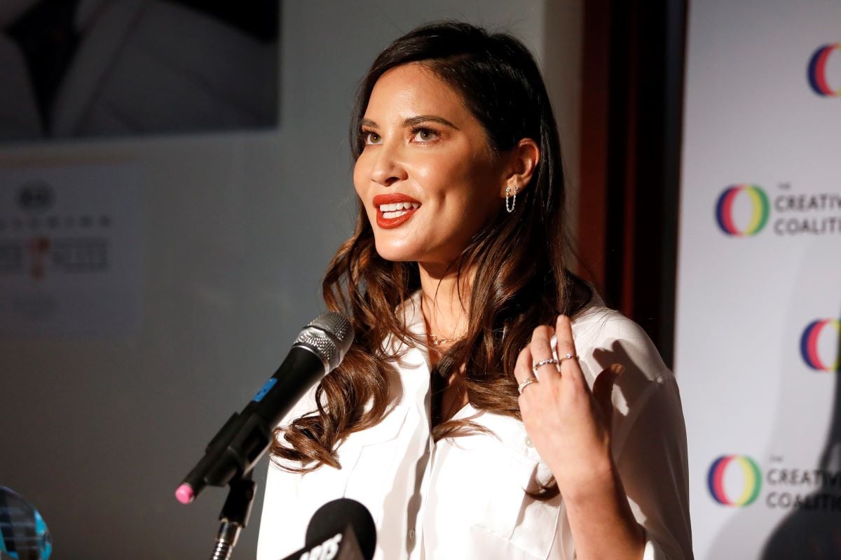 Olivia Munn in white talking into a microphone