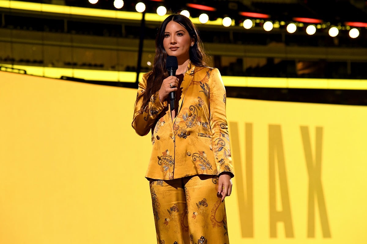 Olivia Munn smirking while wearing a gold dress