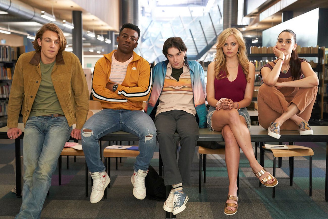 Cooper van Grootel as Nate, Chibuikem Uche as Cooper, Mark McKenna as Simon, Annalisa Cochrane as Addy, Marianly Tejada as Bronwyn pose against a table in the library from the Peacock series 'One of Us Is Lying'